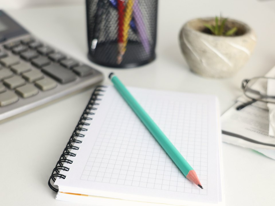 A spiral notebook and pencil beside a calculator on a bright desk, ready for working through questions